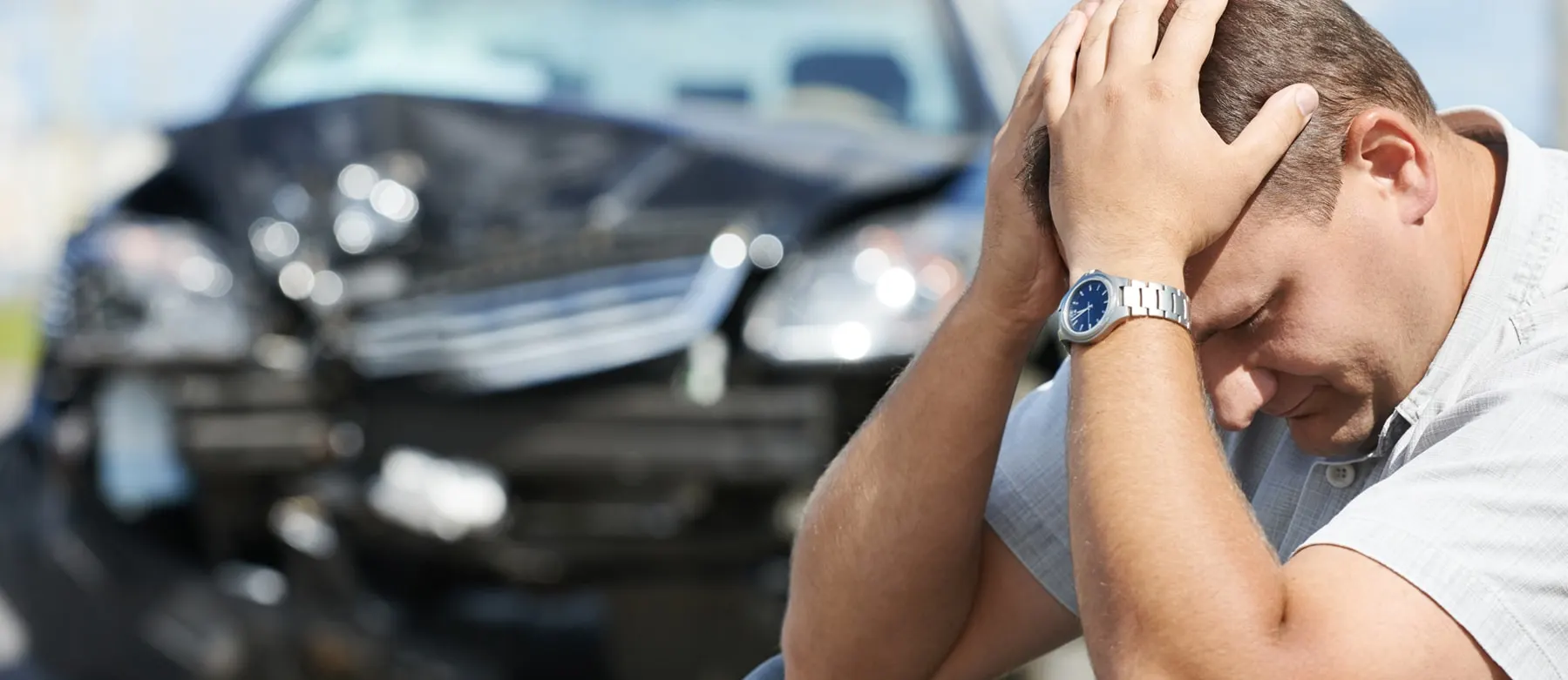 Image montrant un homme pleurant devant sa voiture accidentée.