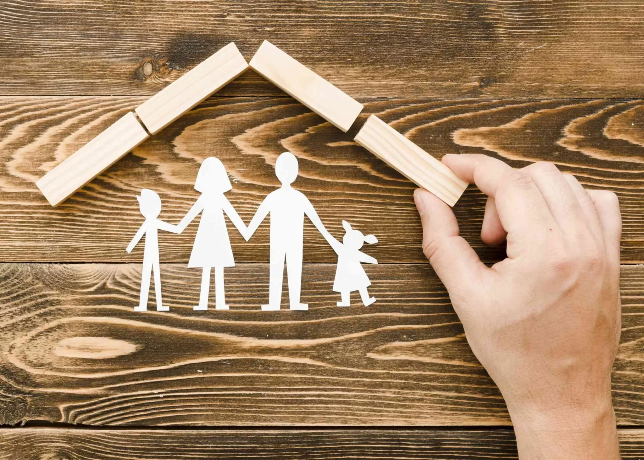 Une main disposant des petit morceaux de bois au dessus d'un papier découpé représentant une famille afin d'illustrer la protection d'un assurance.