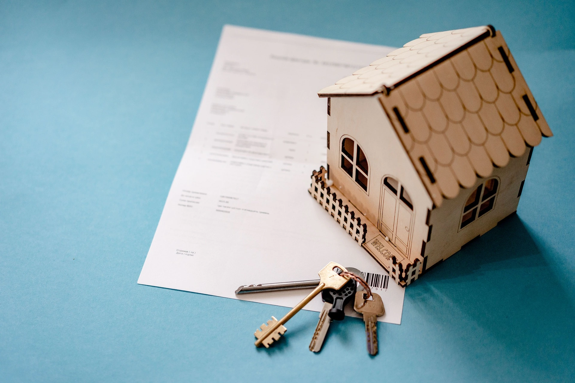 Une maquette de maison en bois posée sur un contrat emprunteur à côté duquel se trouve un trousseau de clés.