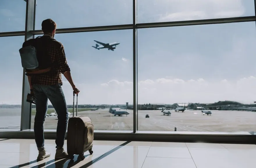 Un homme dans un aéroport regardant un avion décoller, prêt à partir pour le voyage lui aussi.