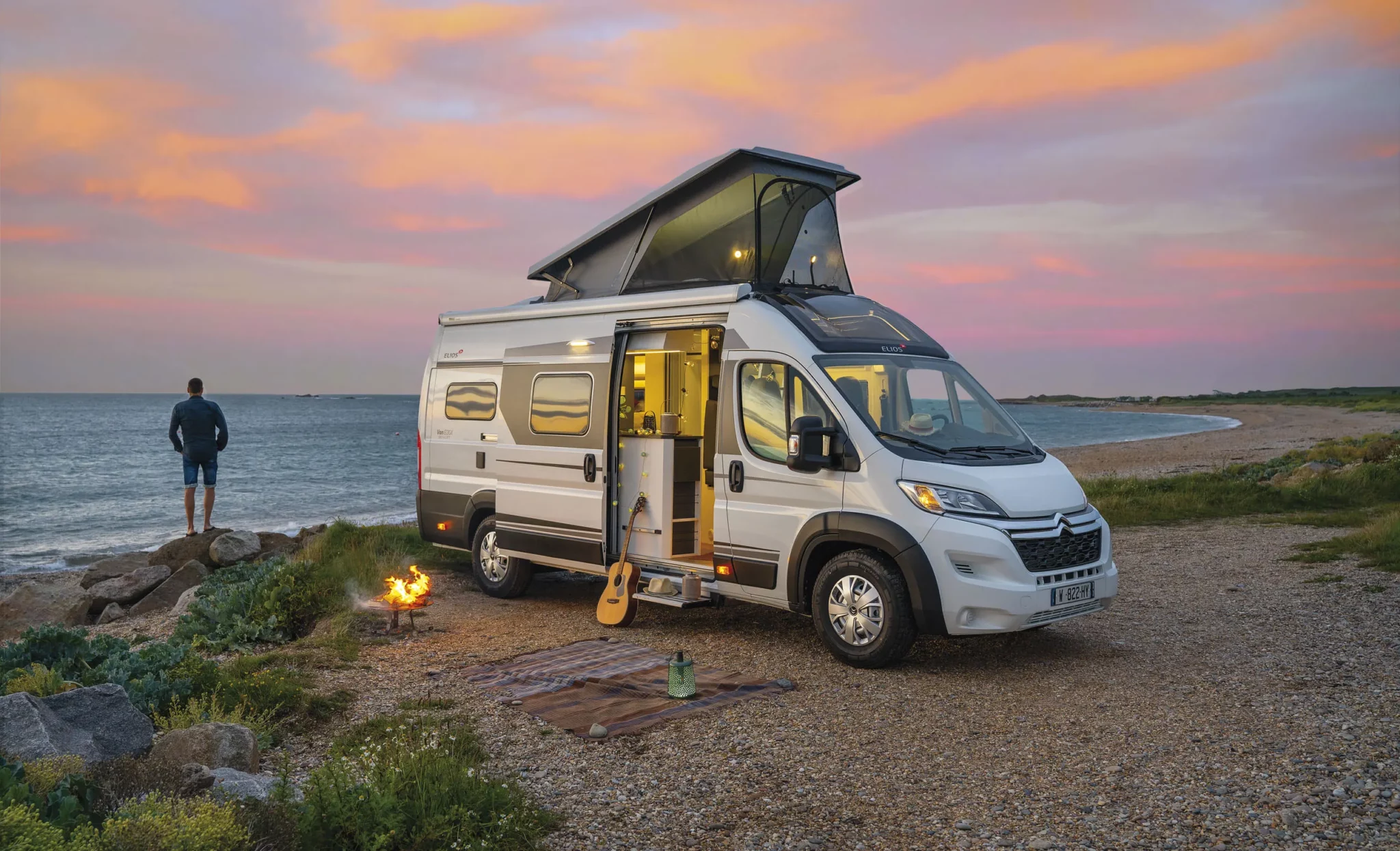 Van aménagé ou petit camping-car garée au bord de l'eau. Un homme, le propriétaire de ce véhicule contemple la mer en début de soirée.