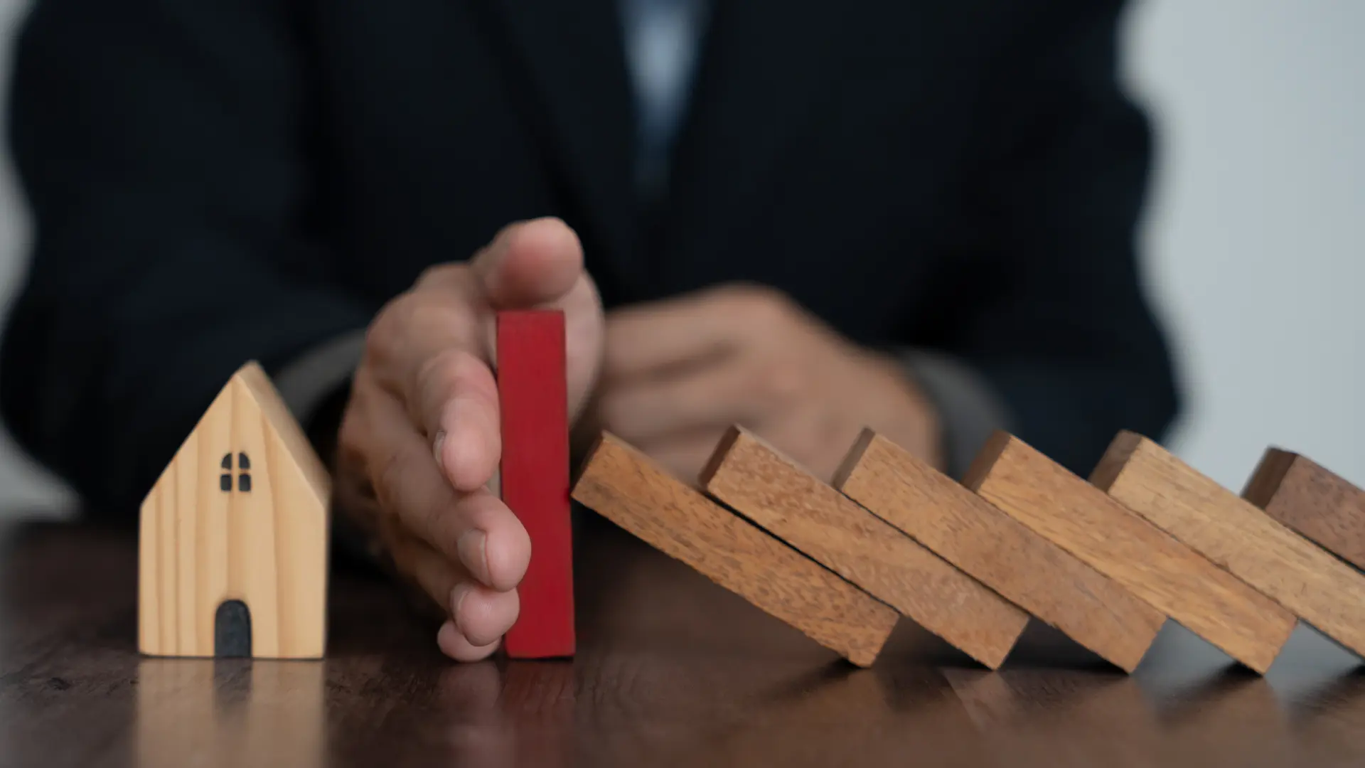 Un assuré à baissé les risques de son contrats d'habituation, illustré par une main qui empêche les morceaux de bois de tomber sur la maison.