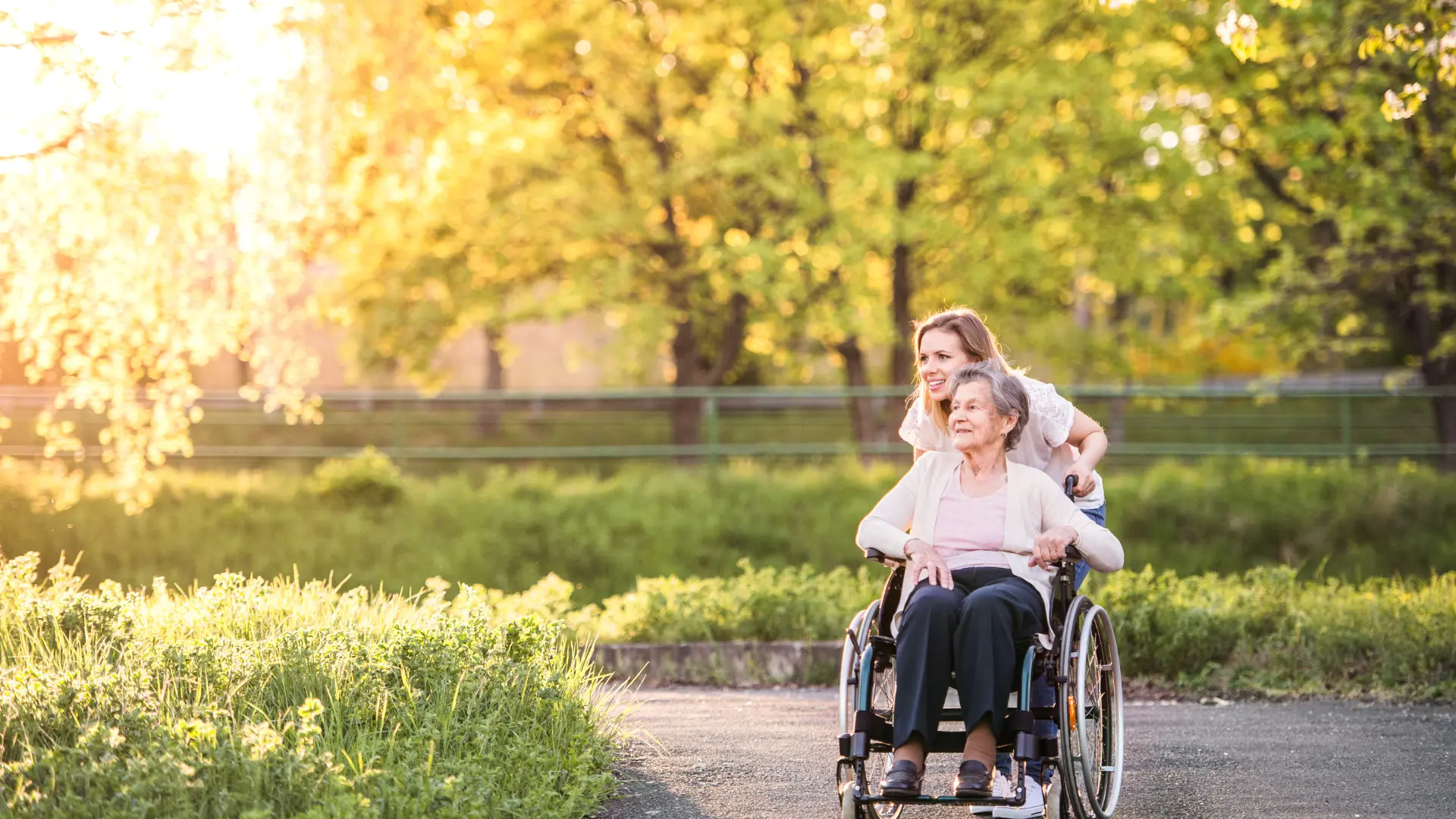 Une personne âgée se faisant promener par son aidant dans un jardin public.